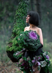 Portrait of a young brunette woman in a creative image. A large head of decorative cabbage and a hat made of cabbage leaves. Art photography.