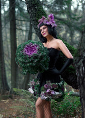 Portrait of a young brunette woman in a creative image. A large head of decorative cabbage and a hat made of cabbage leaves. Art photography.