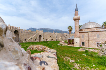 An ancient stone fortress and mosque stand gracefully amid a green field, epitomizing cultural history...