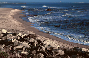 Seascape. Wild beach of Portugal. Waves in motion. Stones washed by water. Abstract background with space for insertion. Wallpaper. Postcard. Poster