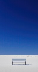 Empty bench on a vast, white expanse beneath a vibrant blue sky