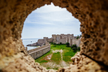 View of a historic fortress through a circular stone opening, showcasing its architectural beauty and green surroundings under a clear sky...