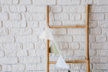 Colorful fabric bunting hanging from wooden ladder against white brick wall