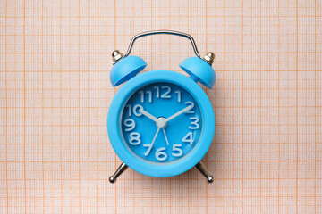 Blue alarm clock on school squared paper background. concept back to school& daily routine of a schoolchild and a student
