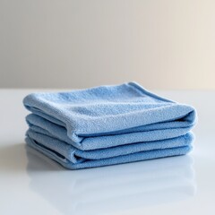 Neatly folded stack of soft blue microfiber cleaning cloths on a glossy reflective surface

