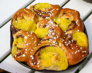 Freshly baked cinnamon rolls filled with sweet yellow cream and topped with sugar sit invitingly on a rustic wooden table, surrounded by a warm, inviting atmosphere