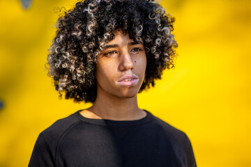 Young woman with vitiligo and curly hair standing in front of yellow background in sunlight