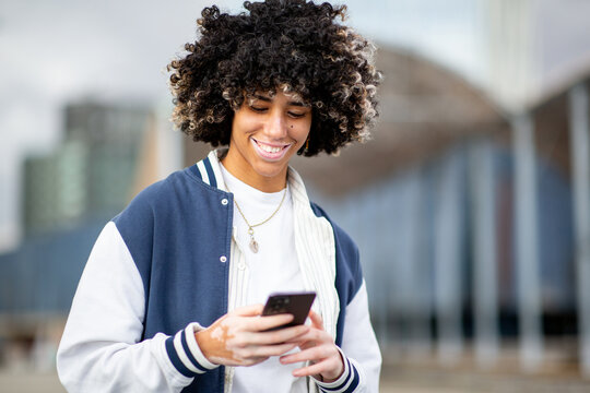 Smiling young woman with skin condition and wearing casual clothes, using smartphone in the city