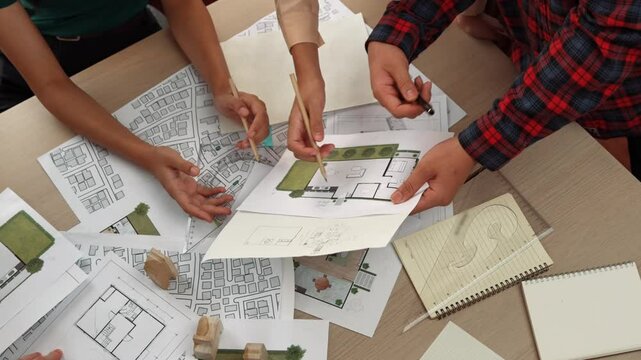 Smart architect and safety engineer discussion about building blueprint on table with architectural document, measurement tools and wooden block scatter around at modern office. Closeup. Delineation.
