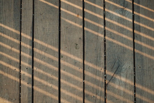 Sunlight filtering across aged wooden planks creates a textured abstract pattern of light and shadow