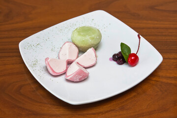 Mochi ice, strawberry and green tea mochi ice accompanied by cherry and blueberries on wooden table