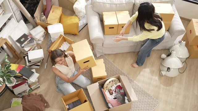 Top view of girl moving the box and sending to her roommate to place at living room surrounded with box. Attractive lesbian moving to new house while helping to move to new house. Girl love. Myrmidon.
