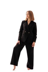 Confident woman in black suit posing barefoot against white background while showcasing modern...