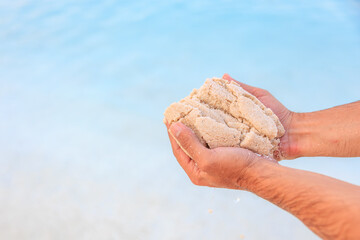 A person is holding a handful of sand on a beach