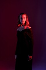 Model poses in an elegant black dress under colorful lighting in a studio during a photoshoot