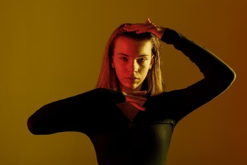 Young woman posing with a dramatic expression and arm gestures against a warm-colored background