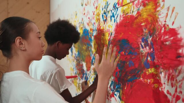 Side view of girl and african boy put the hand in watercolor and stamp on wall. Multicultural children painting color or decorate room with vibrant hand print in art lesson. Creative. Edification