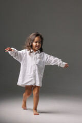 Barefoot child in oversized shirt smiling and walking playfully indoors.