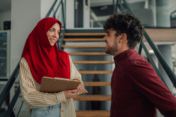 Muslim businesswoman wearing hijab holding clipboard talking to businessman in office