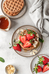 Oatmeal belgian waffles with strawberry, honey and almond petals stacked on a plate, white background. Top view