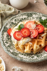Homemade belgian waffles with strawberries, whipped cream and honey close up. Served on a rustic plate with spring flowers
