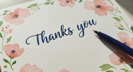 Thank you card with floral design and pen on a tabletop  