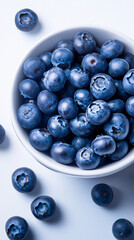Ripe blueberries tumbling from ceramic bowl, scattering across soft blue background with fresh, juicy appeal