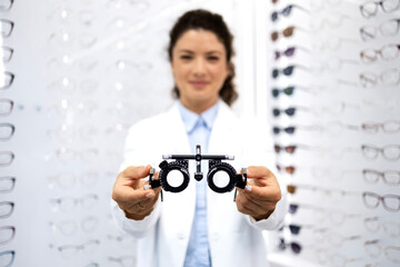 Close up view of female optometrist holding optical instrument for eyesight examination. Focus on test eyeglasses.