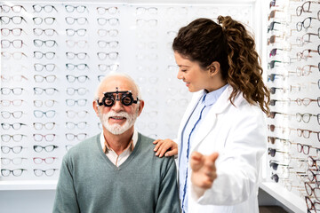 Experienced optometrist checking senior man eyesight focus and diopter using test eyeglasses...