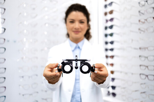 Close up view of female optometrist holding optical instrument for eyesight examination. Focus on test eyeglasses.