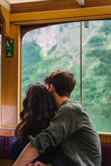 Fototapeta premium The couple sits close together in a train, gazing out at the lush green mountains. Their relaxed posture suggests they are enjoying the serene scenery during their journey. Konigsse Bavaria German