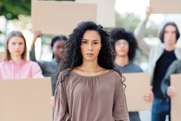 Active pretty young woman leading a group of demonstrators on the street. International diverse group of people with blank placards protesting for human or animal rights and against racism