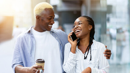 Weekend and shopping. Portrait of african american couple with coffee, smartphone and shopping bags in hands in city mall, free space