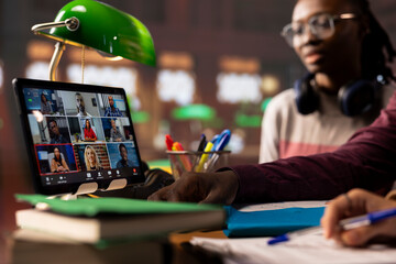 Group of diverse pupils engaging in an online course discussion via video call, participating at the remote class seminar from the campus library. Young people takes notes from academic tutor.