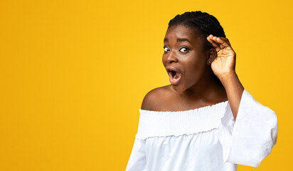 Gossip Concept. Curious african american lady keeping hand near ear, trying to overhear something,...