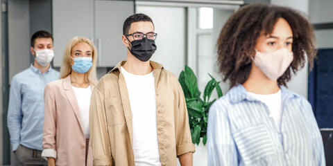 Queue to check temperature before work and new normal after lockdown and social distancing. Multiracial workers in protective masks near office entrance on job during coronavirus epidemic