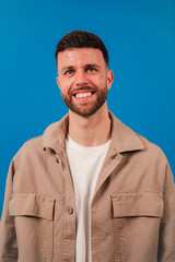 Obraz premium Cheerful young man with a bright smile radiates positivity while posing confidently against a blue backdrop. His joyful demeanor captivates attention and reflects a sense of happiness and