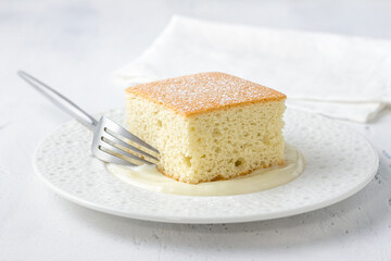 Slice of homemade sponge cake with vanilla sauce on white plate and fork on light background