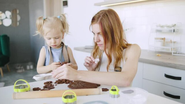 Cooking together brings joy as a mother helps her child make chocolate cookies in a modern kitchen