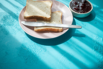 Spreading strawberry jam on toast bread on pink plate in close-up
