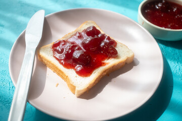 Spreading strawberry jam on toast bread on pink plate in close-up