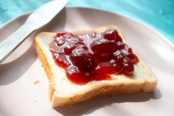 Spreading strawberry jam on toast bread on pink plate in close-up