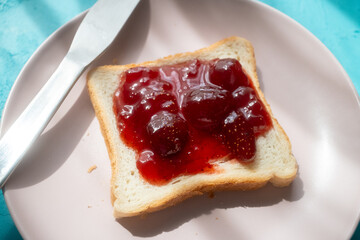 Spreading strawberry jam on toast bread on pink plate in close-up