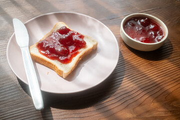 Spreading strawberry jam on toast bread on pink plate in close-up