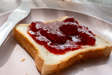 Spreading strawberry jam on toast bread on pink plate in close-up