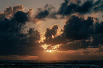 view of a tropical landscape with the sun shining through the clouds on a colorful sunset