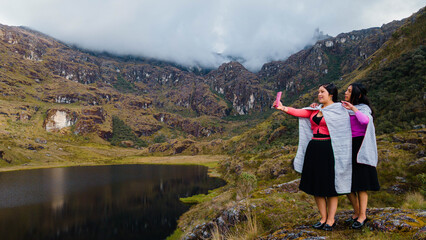 Naklejka premium par de Mujeres quechuas con vestimenta tradicional en América Latina, feliz mientras usa un teléfono inteligente mirada a un espacio publicidad y aislada en un fondo naturaleza,celular.Quechua.