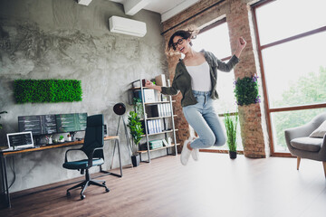 Young woman jumping happily in modern home office workspace with computer and programming setup
