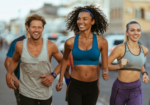 Group of fit friends running together outdoors on city street