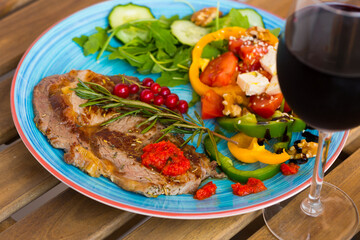 Roasted veal steak with vitamin salad from arugula, cucumber, tomatoes, bell pepper, feta cheese and walnuts on wooden surface